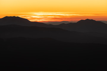 Orange and yellow sunset with mountains silhouettes. Gradient vivid nature background.