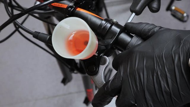 A close up view of bleeding brake of bicycle lever by cup, screwing and checking brake, Wearing black gloves in hands.
