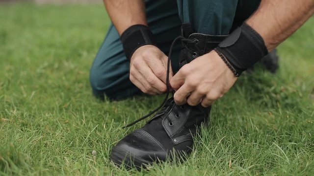 Close-up. Male hands tying shoelaces of his high black leather boots outdoors