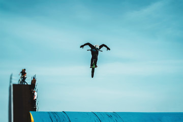 Silhouette of a unrecognizable young bike rider performing aerial BMX trick against blue sky. Extreme sport, youth culture