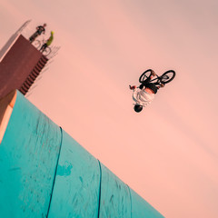 Young unrecognizable Bmx rider performing air trick back flip. Extreme sport. Intentional angle to the horizon