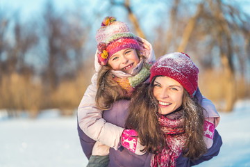 Little girl and her mother playing outdoors at sunny winter day. Active winter holydays concept.
