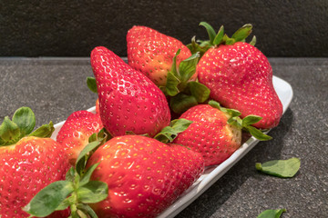 large ugly strawberries in a white plate on a dark stone table.