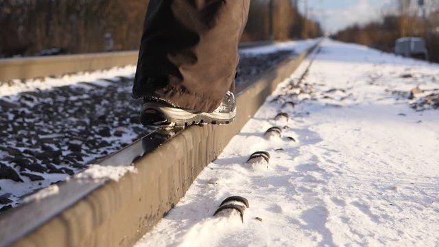 Girl enjoy sunny winter day, walk at steel rail, low camera show warm sportive shoes stepping on slippery metal track, blurred railway perspective on background. Light snow lie around, slow motion