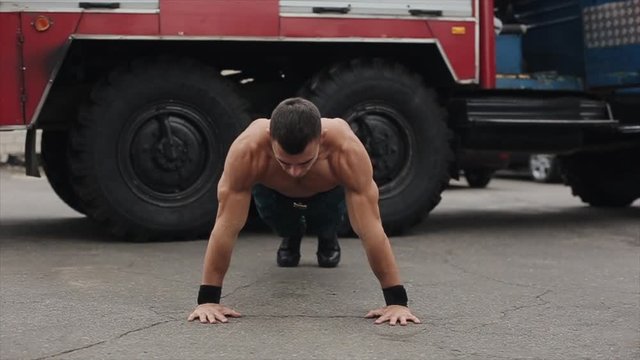 Handsome young sportsman doing push-ups with claps outdoors with a fire truck in the background