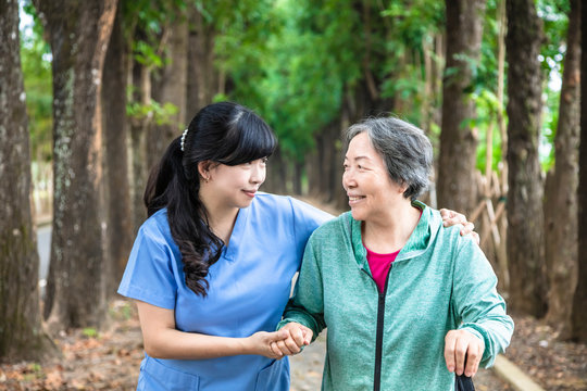 Smiling nurse helping senior woman to walk around the park