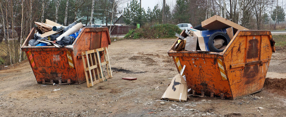 Crushed rusty orange color garbage containers  filled with construction debris near the village road