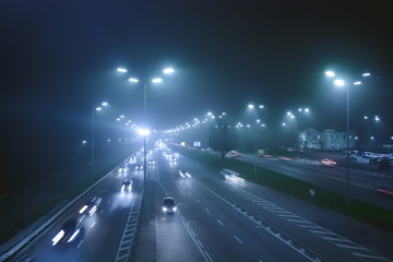 Cars on the night motorway in a fog. Highway in a foggy night with street lights and signs on the asphalt