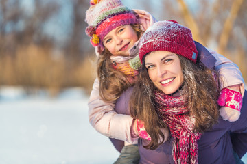 Little girl and her mother playing outdoors at sunny winter day. Active winter holydays concept.