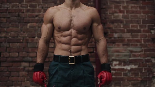Sexy sportsman with naked torso shows his muscles over red brick wall background. Close-up