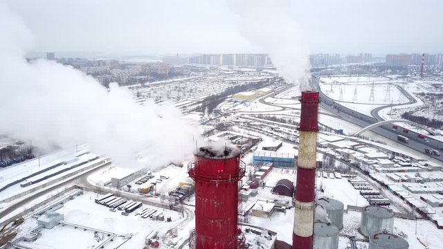 Carbon dioxide and water vapour curl away from two tall chimneys, aerial shot. Winter season, industrial area covered with snow. Camera stay close to outlet at top of stack. White clouds whirl out
