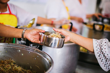 The hand of the wanderer extends to receive food from donations. With volunteers scooping food: the idea of helping with hunger