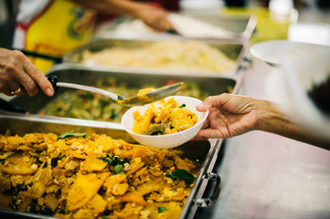 The hand of the wanderer extends to receive food from donations. With volunteers scooping food: the idea of helping with hunger