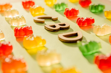 Wooden letters CBD on a green background and gelatin in the form of bears. View from above. The shadow of the sun falls on the background