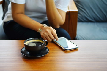 Fototapeta na wymiar A hot coffee in a black mug is placed in frort of a woman texting on her cell phone.