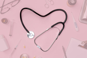 Stethoscope in shape of heart with medical documents, thermometer, syringe and pills on pink table...