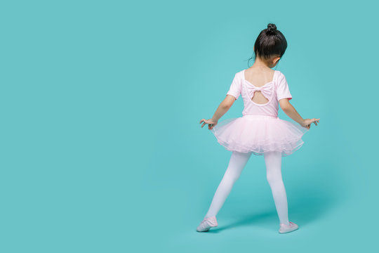 Beautiful smiling Asian little girl in a pink suit is dancing a ballet at school, empty space in studio shot isolated on colorful blue background