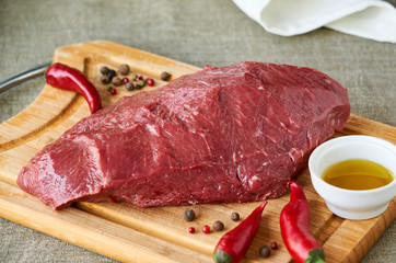 Piece of raw beef with spices and oil on a wooden cutting board