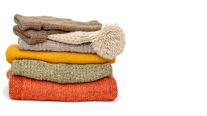 A stack of folded knitted warm women sweaters, hat and gloves on a white background. Season of warm clothes. Time to keep warm. Closeup. Copy space