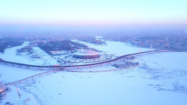 Krestovsky Stadium and Western Rapid Diameter highway road, aerial panoramic shot of frozen Neva Bay waters in winter evening. Blue color tint of cityscape after sunset, cold weather, snow lie around
