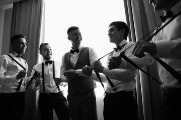 Black and white wedding photography. Groom smiling when groomsmen pull up the suspenders