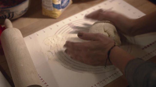Hands knead and roll dough in flour on butcher block counter with rolling pin, high angle