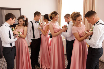 Group wedding photography. Wedding tradition. Bridesmaids put small bouquets on suspender of...