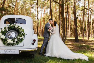 Wedding couple kissing near just married car with bouquet and the word "Wedding". Car for the bride and groom