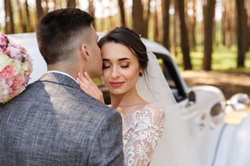 Bride and groom kisses near white just married car at wedding day