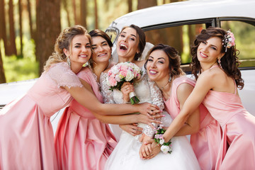Wedding photography of happy bride and bridesmaids in pink dresses embracing with smile on wedding...