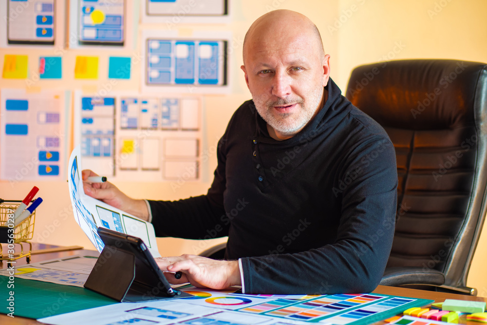 Poster designer is looking at the camera. ux designer. man at the desk. office designer mobile applications