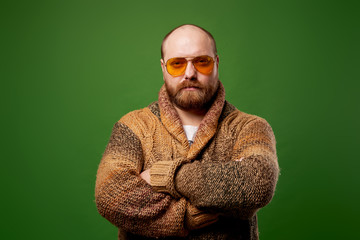 Bald male in sweater with arms crossed on empty green background