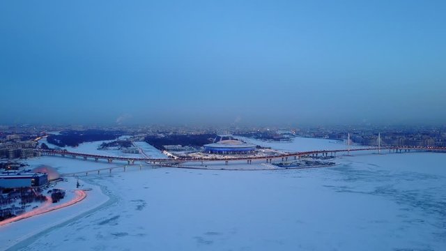 Krestovsky Island aerial panoramic view from Neva Bay side, winter season frozen Gulf of Finland water covered with ice and snow. Evening twilight, Zenit Arena stadium and Western Rapid Diameter road