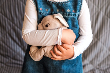 Little girl holding her rabbit toy close up on gray background.