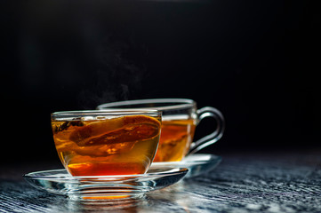 Freshly brewed tea in a transparent glass cup, escaping steam, darker background.