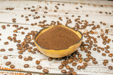 Natural bowl with ground coffee on white wooden table with organic coffee beans