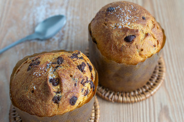 Top view of two panettones with unfocused spoon, on wooden board with sugar grains horizontal