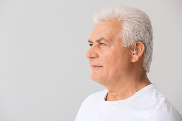 Mature man with hearing aid on light background