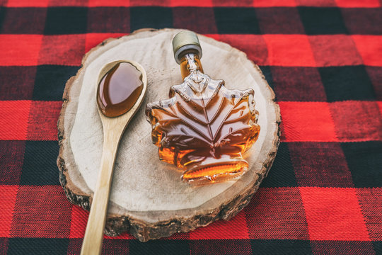 Maple syrup bottle Quebec cultural food traditional harvest top view on buffalo dining tablecloth background. Canada grade A amber sweet liquid in wooden spoon from sugar shack cabane a sucre farm.