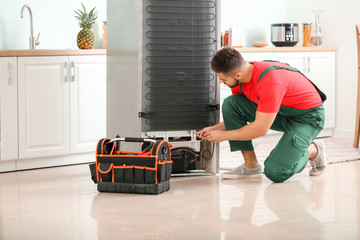Male technician repairing refrigerator in kitchen