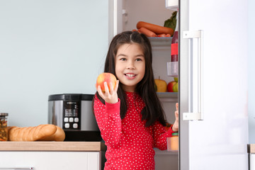Fototapeta na wymiar Little Asian girl choosing food from fridge in kitchen
