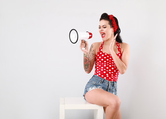 Portrait of beautiful tattooed pin-up woman with megaphone on light background