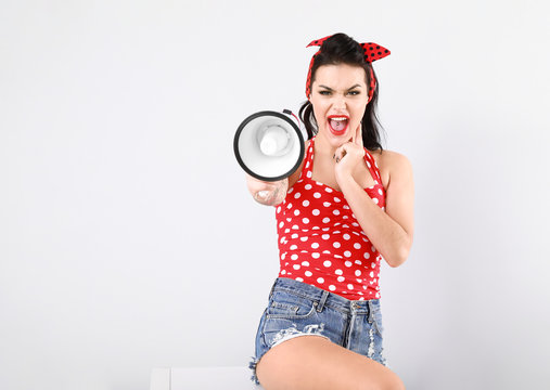 Portrait of angry tattooed pin-up woman with megaphone on light background