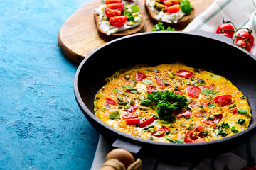 Fresh Breakfast in the pan. Omelette with greens and tomatoes, sandwiches with cream cheese, pesto and cherry tomatoes on a turquoise background with copy space