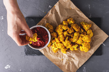 hand waving cauliflower in tomato sauce on black stone Board on gray background