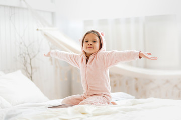 child in plush pajamas on bed, light bedroom