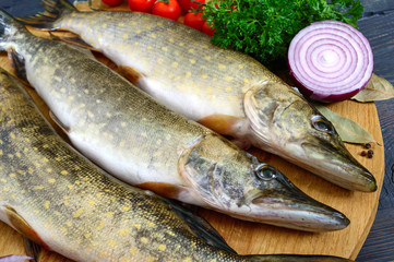 Big raw pikes with vegetables and herbs on a wooden tray. Fresh catch. Dietary product. Ready to cook.