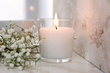 Burning candle, notebook and flowers on table
