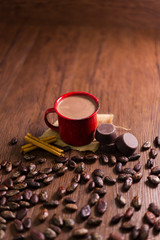Red cup with hot chocolate on wood and surrounded by cocoa beans, pieces of pure chocolate and cinnamon - pewter cup top view