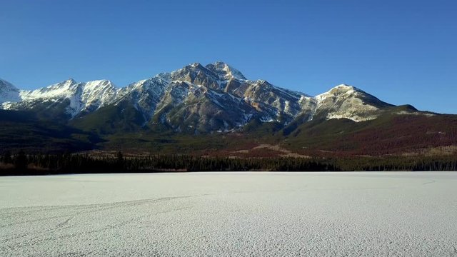 Drone flight over a frozen lake towards a snow covered mountain in Jasper, Canada
